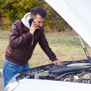 discontented man talking on the phone and looking under the hood of breakdown car at outdoor